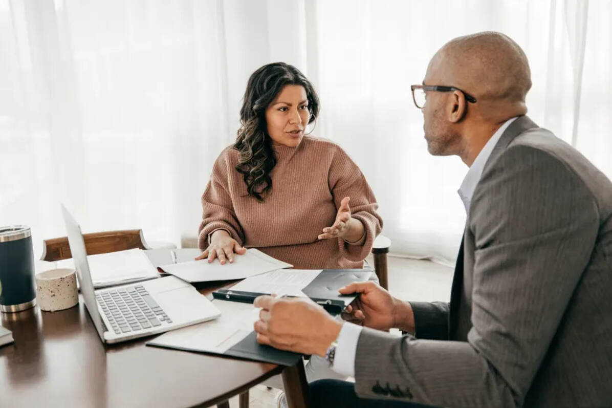 Two people discussing at a table with papers and a laptop